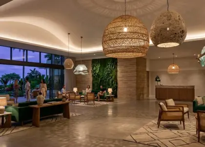 A panoramic view of a luxury hotel lobby with a biophilic design, featuring large organic-textured pendant lights, a green living wall, and a gold RST logo on a wood-paneled wall behind the reception desk.