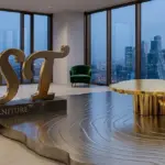 Gold-plated nested coffee table with tree-ring engraved metal floor and brass RST logo at dusk, overlooking a city skyline through large windows.