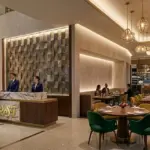 A luxury modern hotel lobby and upscale restaurant interior featuring a marble reception desk with the gold RST logo, a spiral crystal art installation, and designer pendant lighting.