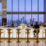 A row of RST Luxury Gold Sculptural Bar Stools with organic metallic frames at a glowing marble bar in a high-end skyscraper sky lounge at twilight.