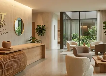 A wide-angle panoramic view of a luxury hotel lobby featuring organic hospitality decor, a minimalist wooden reception desk, and the RST logo mounted on a textured concrete wall.