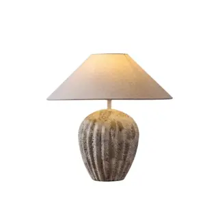 Hand-carved stone texture ceramic table lamp with vertical grooves and beige conical shade for luxury hotels.