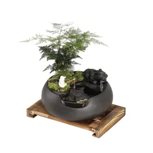 Artisanal Zen ceramic water fountain with miniature fisherman and asparagus fern on a wooden base.