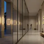 RST architectural alabaster wall sconces with honeycomb texture illuminating a luxury hotel lobby and exterior facade at dusk, featuring a golden RST logo on a textured concrete wall.