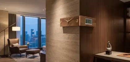 A modern natural wood corner wall clock with analog and digital displays mounted on a corner wall in a luxury professional interior.