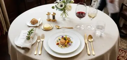 Top-down view of fine bone china tableware, gold cutlery, and crystal glassware on a luxury hotel dining table.